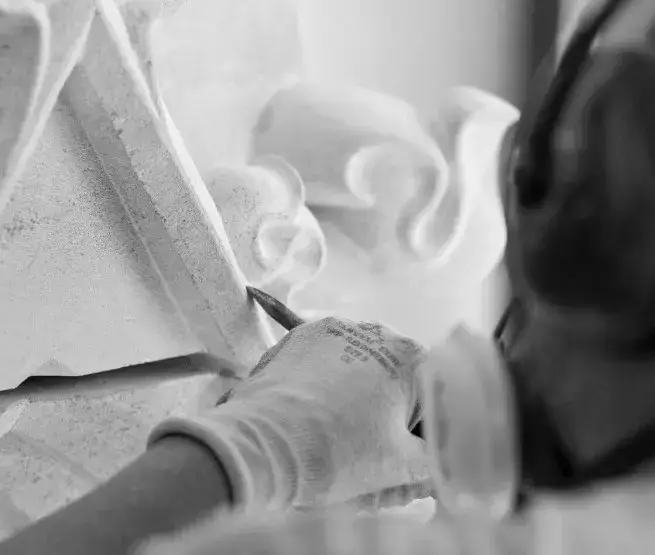Restauratiemedewerker die met fijn handgereedschap natuursteen bewerkt aan een ornamenteel geveldetail, onderdeel van een gespecialiseerd restauratieproject.