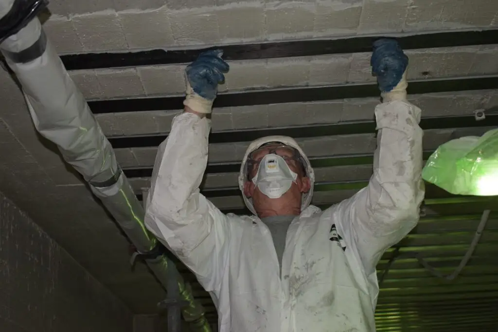 Handmatige plaatsing van gelijmde wapening aan de onderzijde van een betonnen vloerplaat, waarbij versterkingsstroken tegen het plafond worden bevestigd voor structurele versteviging van de betonconstructie.